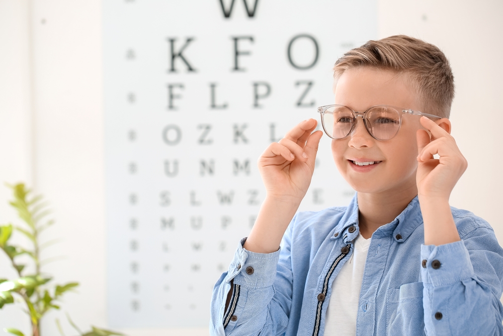 An optometrist helps a patient try on glasses while sitting at a desk with a computer displaying eyewear options - Eye Doctor in Grand Rapids MI