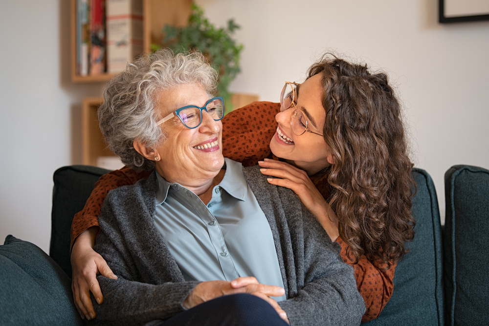 An optometrist helps a patient try on glasses while sitting at a desk with a computer displaying eyewear options - Carlson Eye Care Grandmother and granddaughter at home - Eye Doctor in Rockford