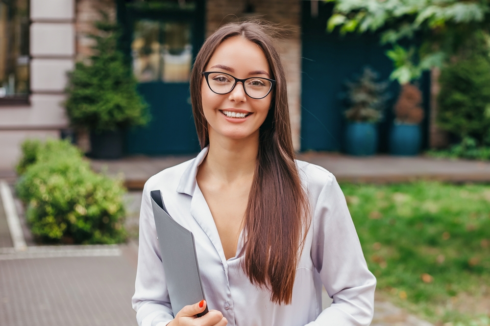 An optometrist helps a patient try on glasses while sitting at a desk with a computer displaying eyewear options - Carlson Eye Care